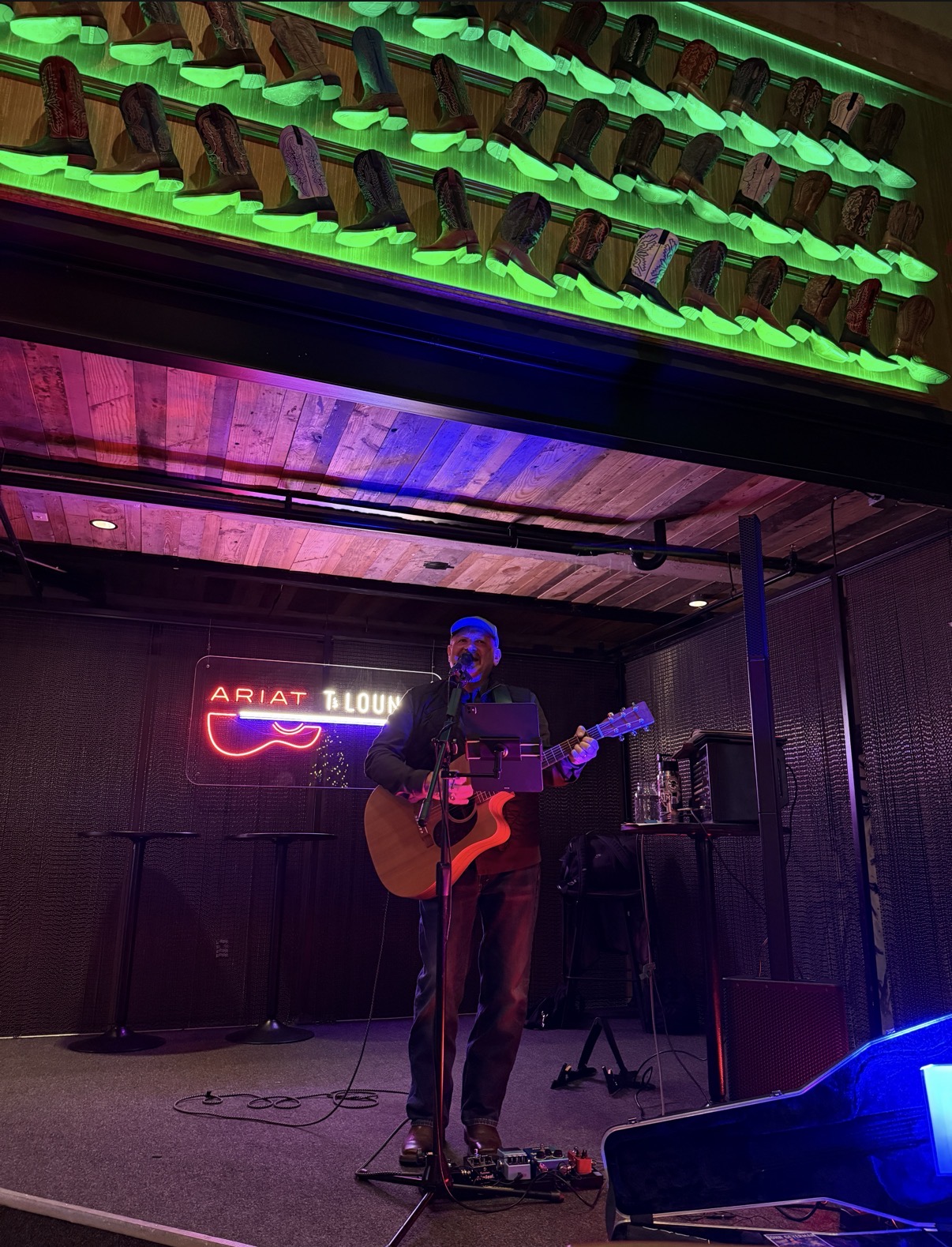 John performing with acoustic guitar beneath illuminated cowboy boots in the Ariat Lounge
